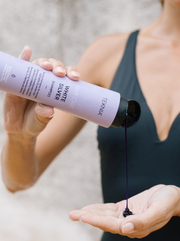 mujer aplic&aacute;ndose el champ&uacute; Teknia White Silver en la mano